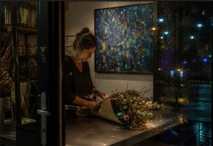 Florist arranging dried stems behind rain-marked glass at night